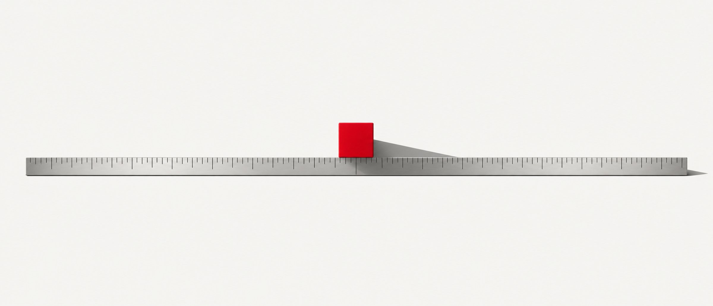A single red cube sitting on a metal ruler, isolated against a plain background.